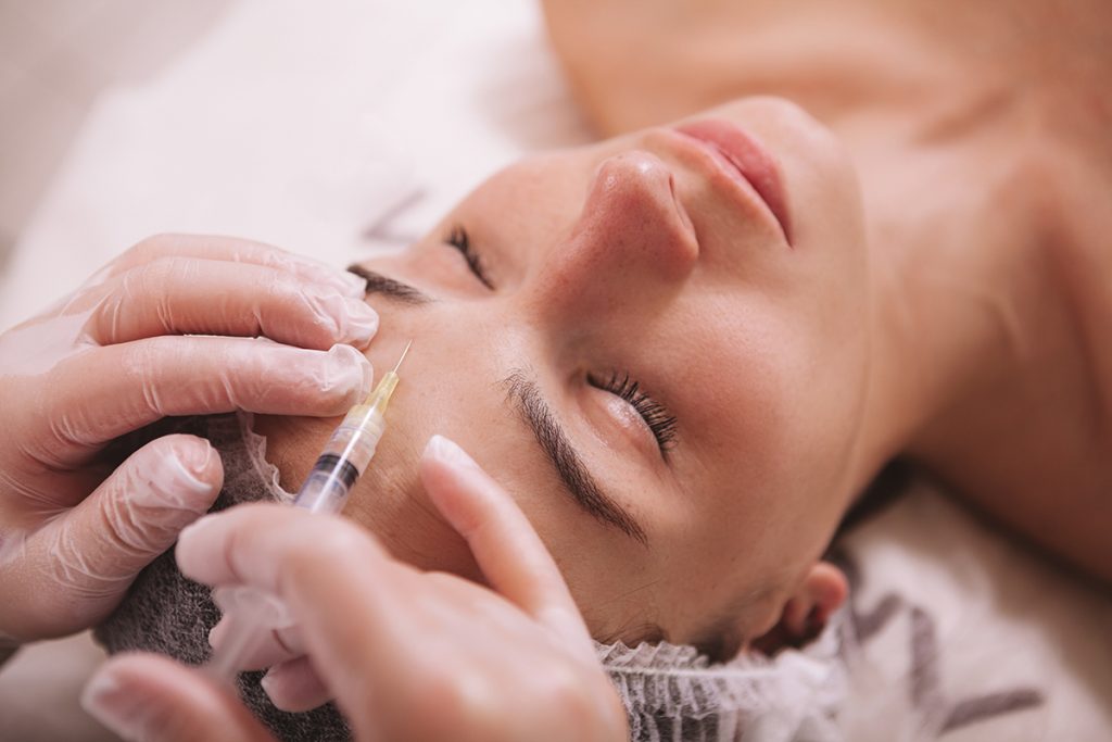 reclined person receives botox injection between the eyebrows