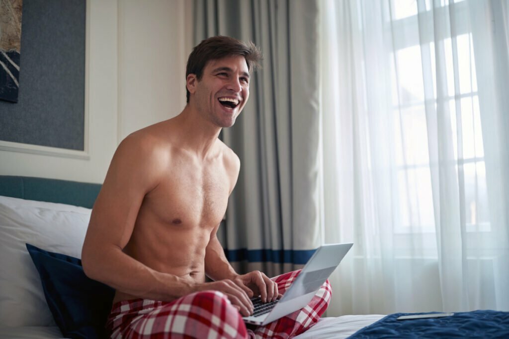 Shirtless man on bed with laptop